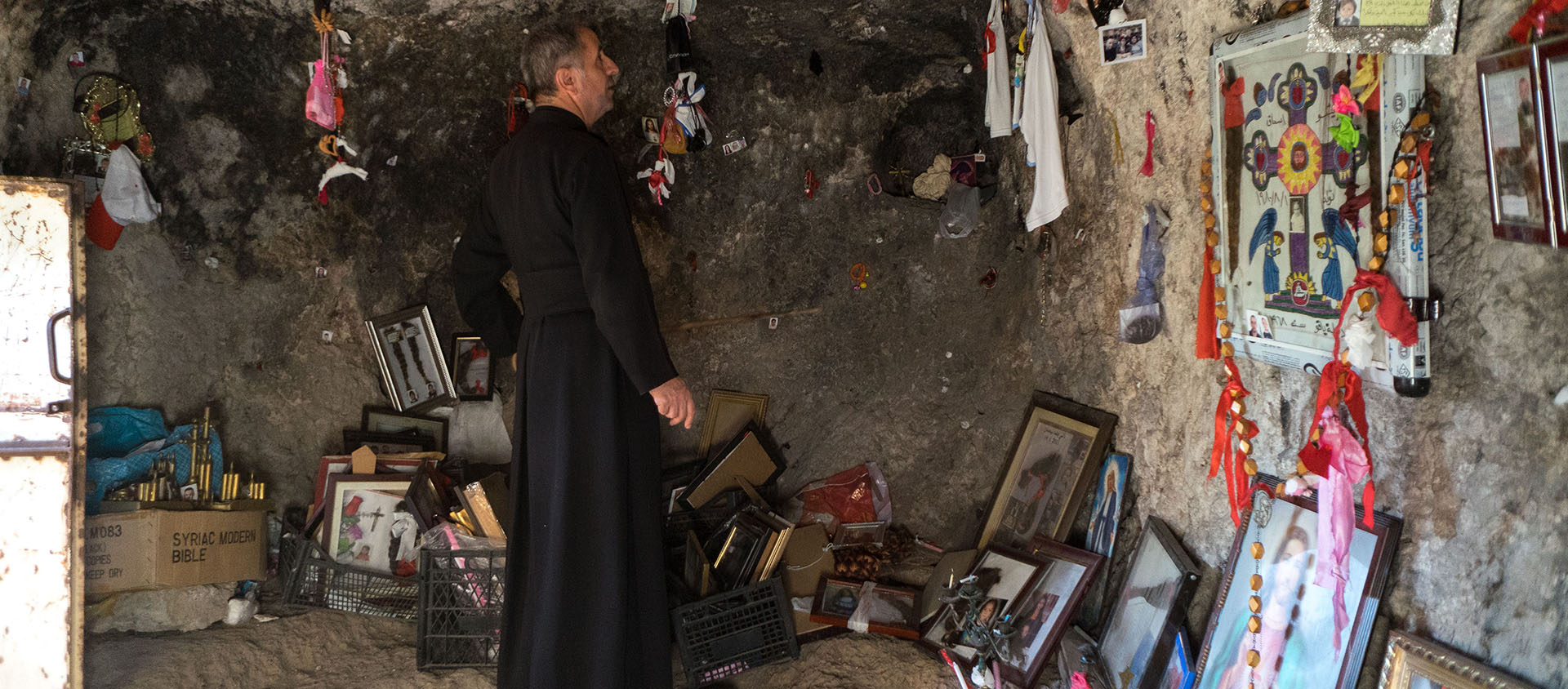 Le père Emmanuel Denkha dans la grotte de Mar Audicho' à Déré avec les offrandes des fidèles, en septembre 2017 | © Pascal Maguesyan
