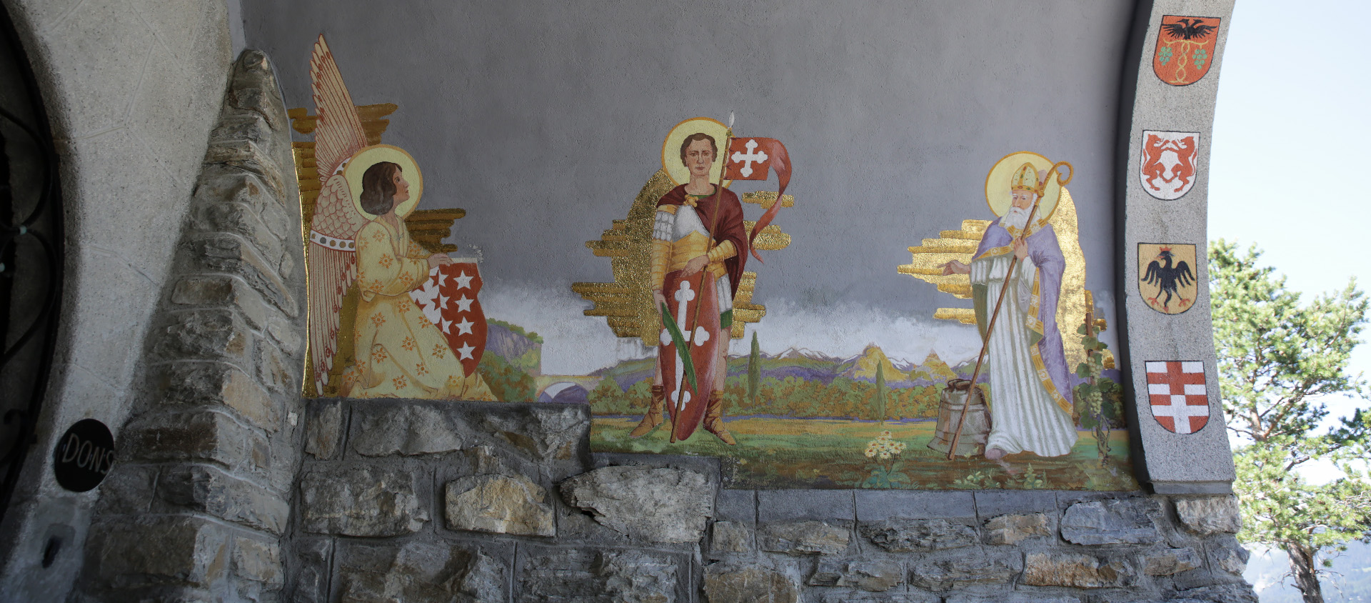 St Théodule une cloche à ses pieds (à dr.), et un pied de vigne à sa gauche, côtoie saint Maurice (centre) sur cette fresque qui borde l'oratoire du Christ-Roi situé au-dessus de Lens (VS) | © Bernard Hallet